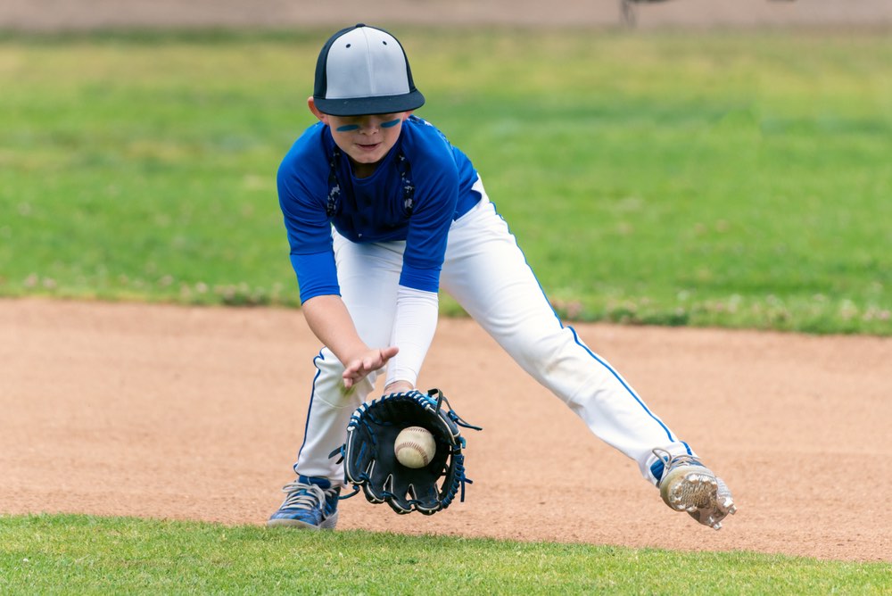 Youth player fields ground ball with baseball glove.