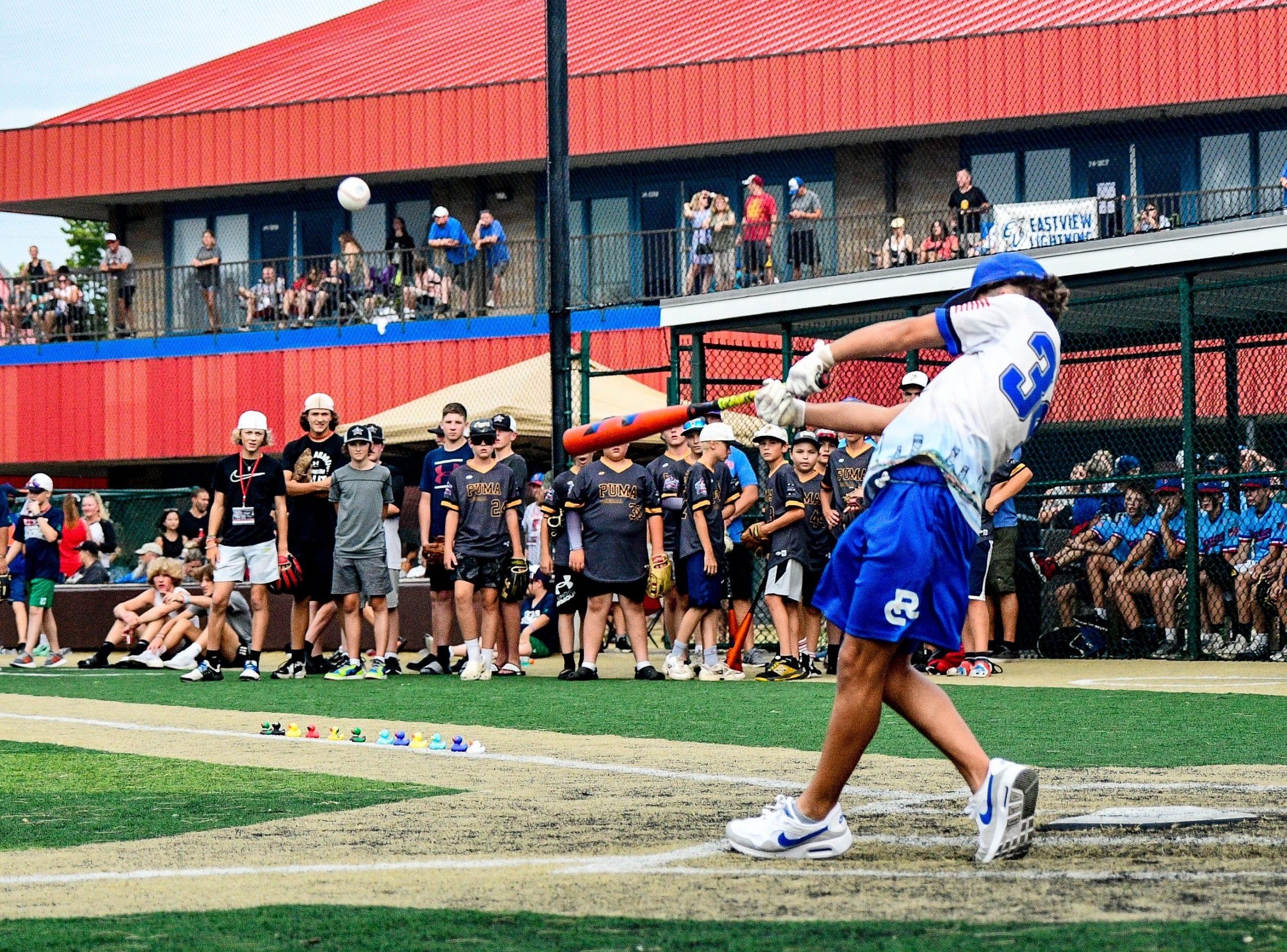 A baseball player wearing a blue and white uniform swings a baseball bat at home plate during the Home Run Derby