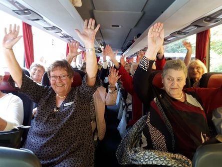 Glade passagerer i en turistbus, der løfter hænderne og nyder turen