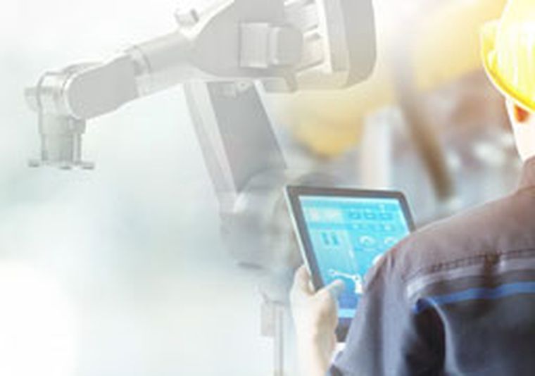 Roboter im Hintergrund, im Vordergrund steuert eine Person mit einem Bediengerät den Roboter