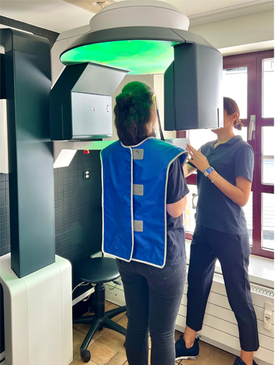 A dental assistant positions a patient wearing a lead apron in front of the Seethrough Max in a dental clinic. A dental assistant positions a patient wearing a lead apron in front of the Seethrough Max in a dental clinic.