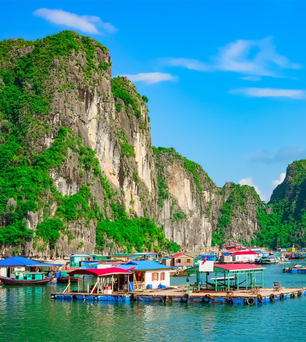 Many floating homes situated next to each other in calm waters surrounded by tall rocky islands