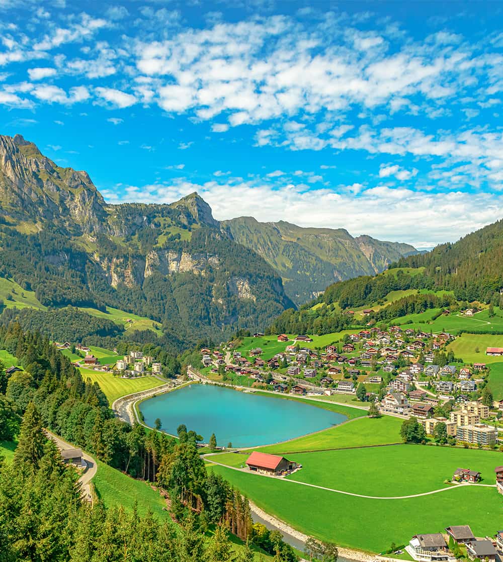 Aerial view of a town on a bright blue lake surrounded by green hills and mountains in the background