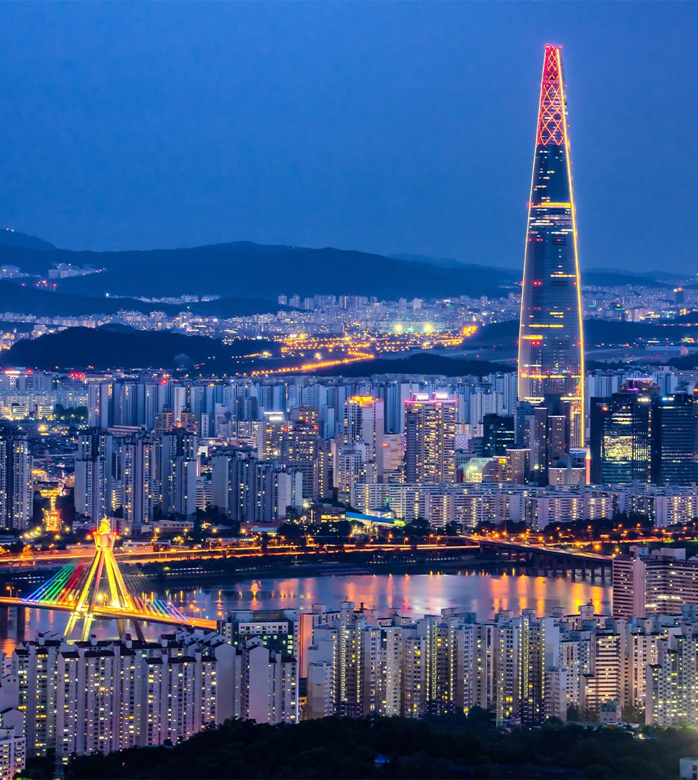 An aerial view of a massive urban city with an extremely tall skyscraper in the center lit up at night