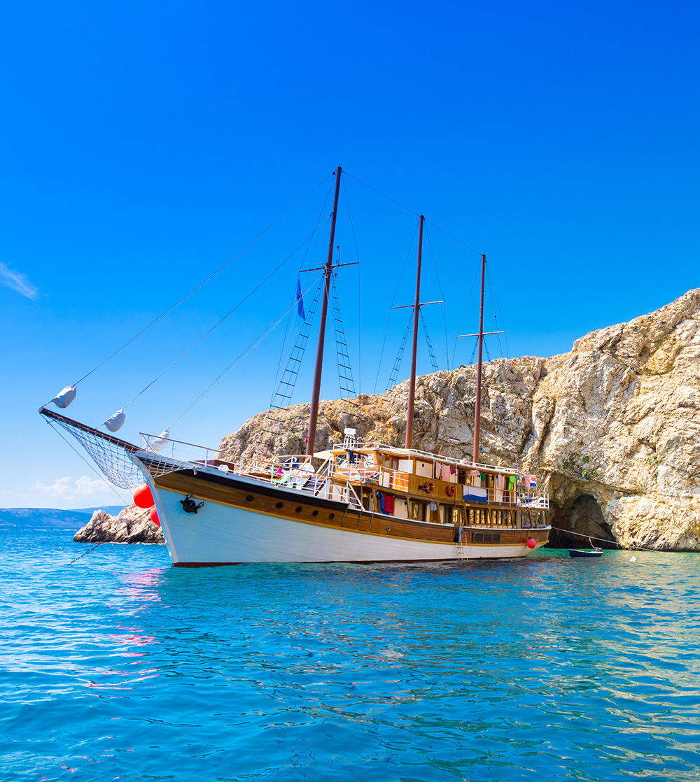 A boat in calm ocean water next to a large rock formation and a secluded beach