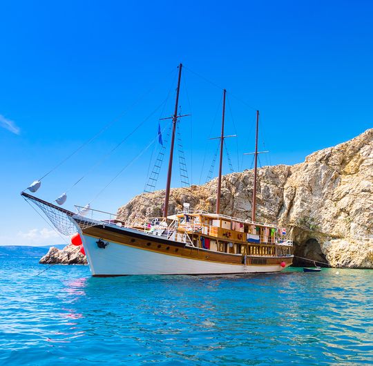 A boat in calm ocean water next to a large rock formation and a secluded beach