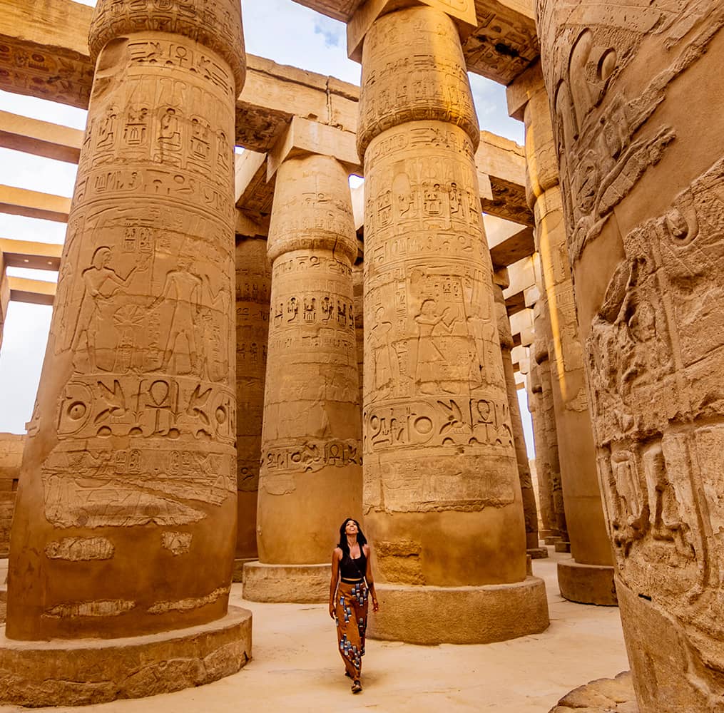 A person walking amidst tall columns decorated with hieroglyphics