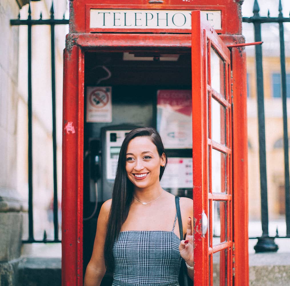 A woman smiling while standing inside a red telephone booth in London