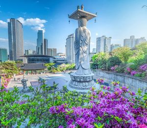 A stone statue in the middle of a flower garden with skyscrapers in the background