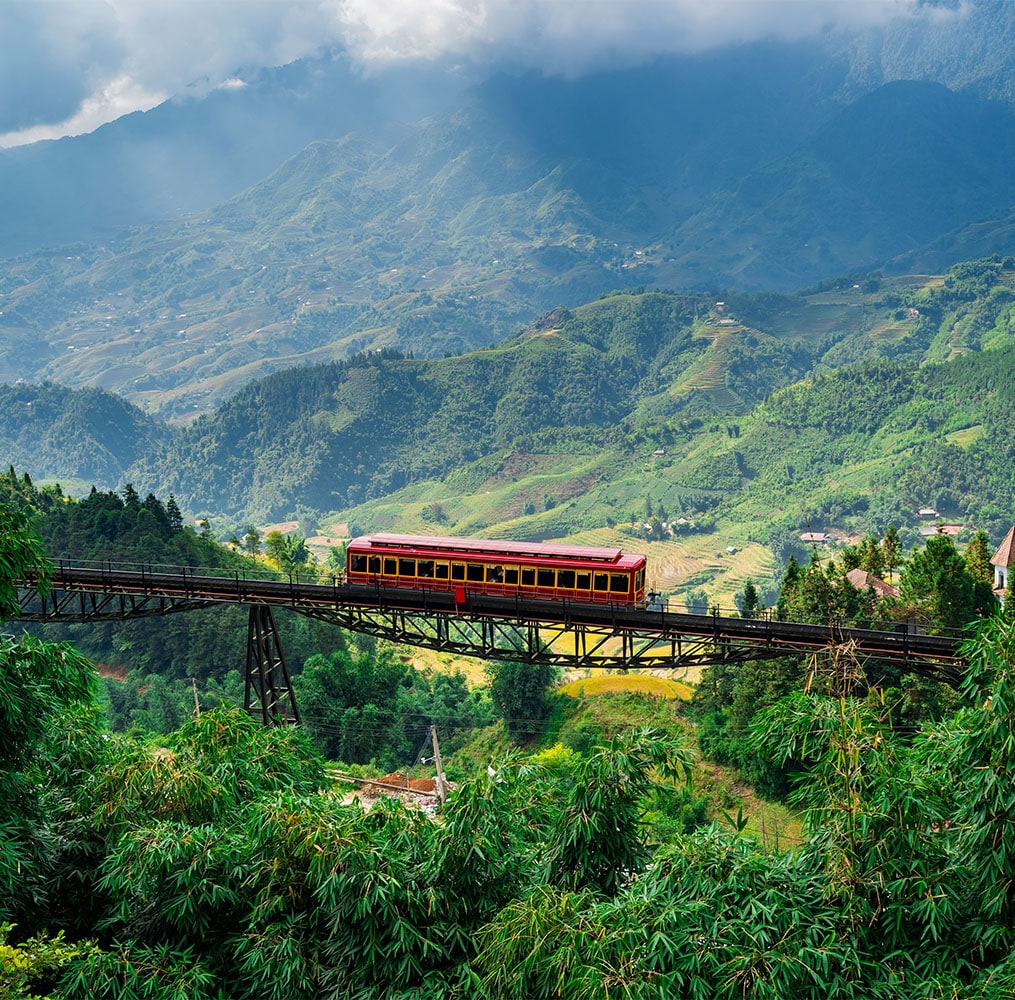 A red train traveling on a bridge surrounded by a lush green forest