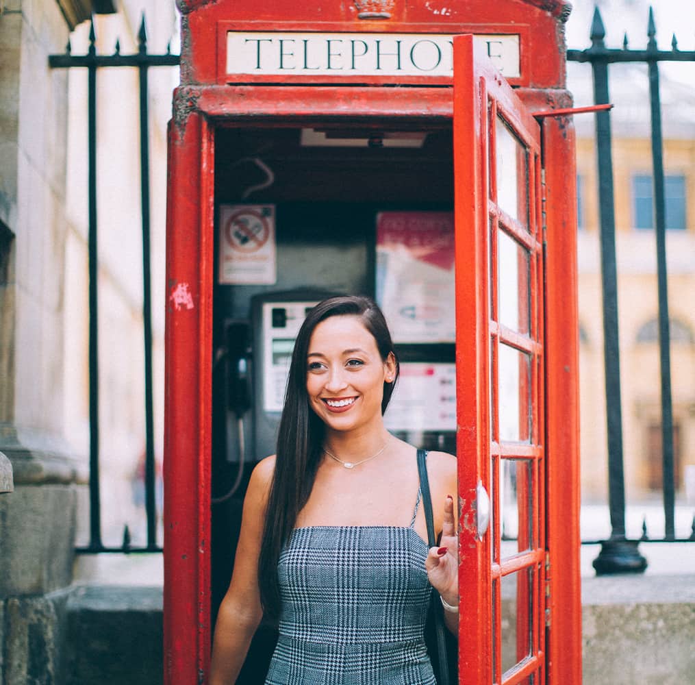 A woman smiling while standing inside a red telephone booth in London