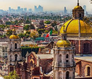 Aerial view of an ornate stone building topped with gold domes and crosses with a cityscapes in the background