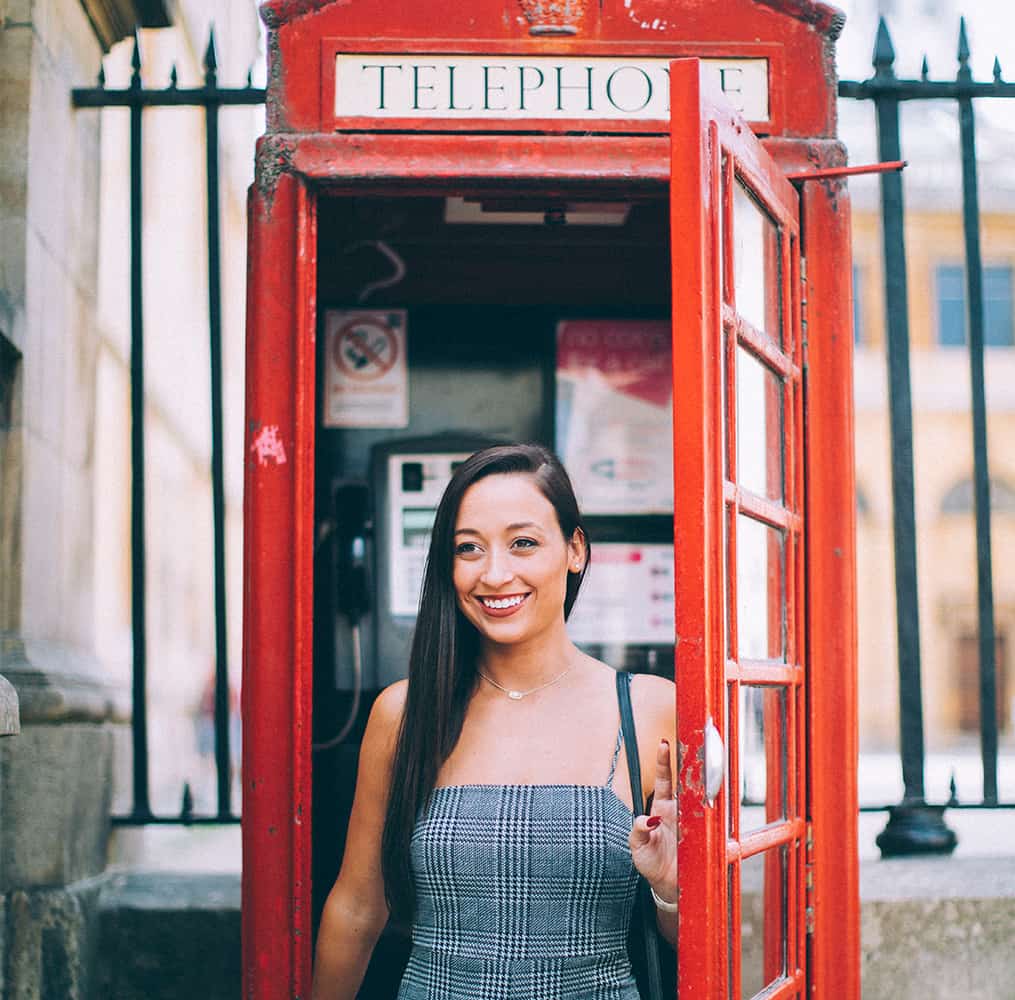 A young woman exiting a red telephone booth