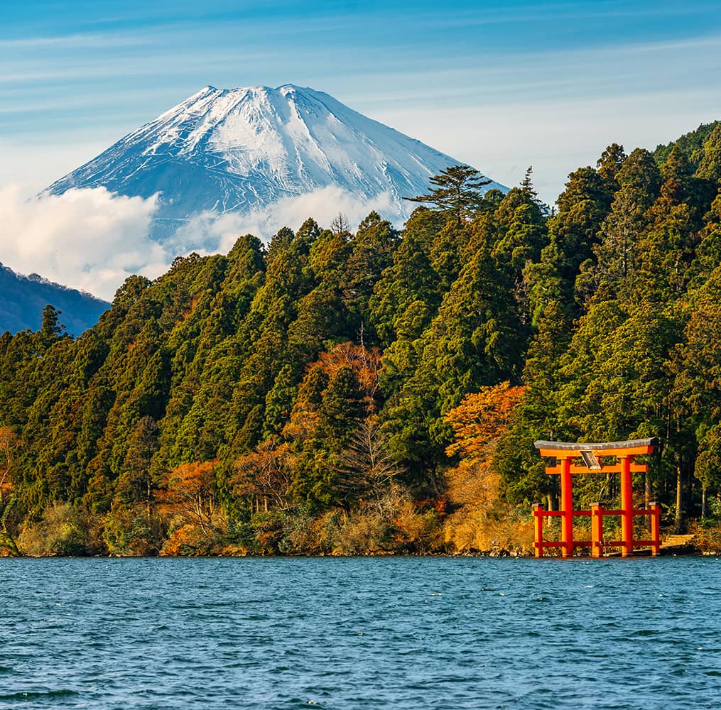 A body of water with trees and a red arch along the shoreline with a snow-capped volcano in the background