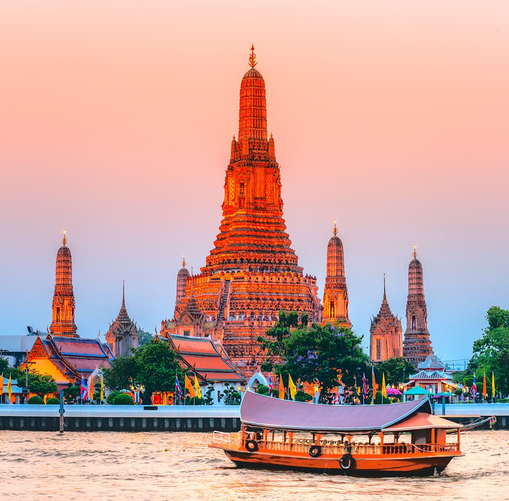 An extremely tall and large temple that is ornately decorated with gold detail situated next to the water during sunset