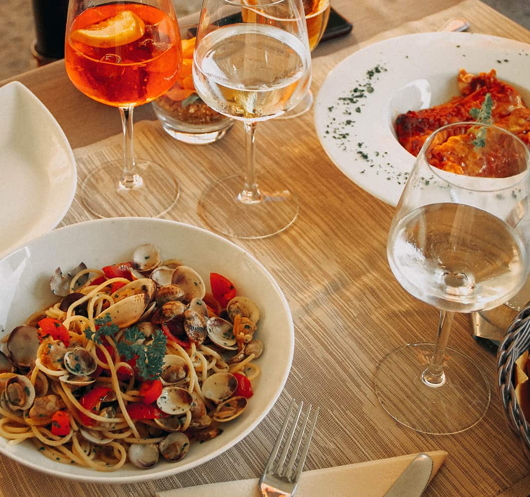 Two pasta dishes on a table with a glass of white wine and an orange cocktail