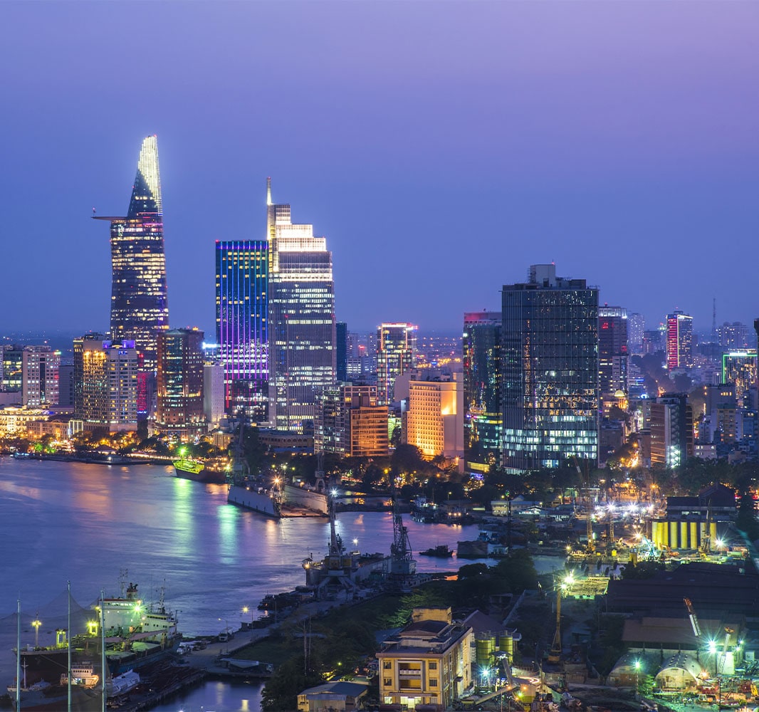 A nighttime view of an urban city with lit up skyscrapers located next to the sea