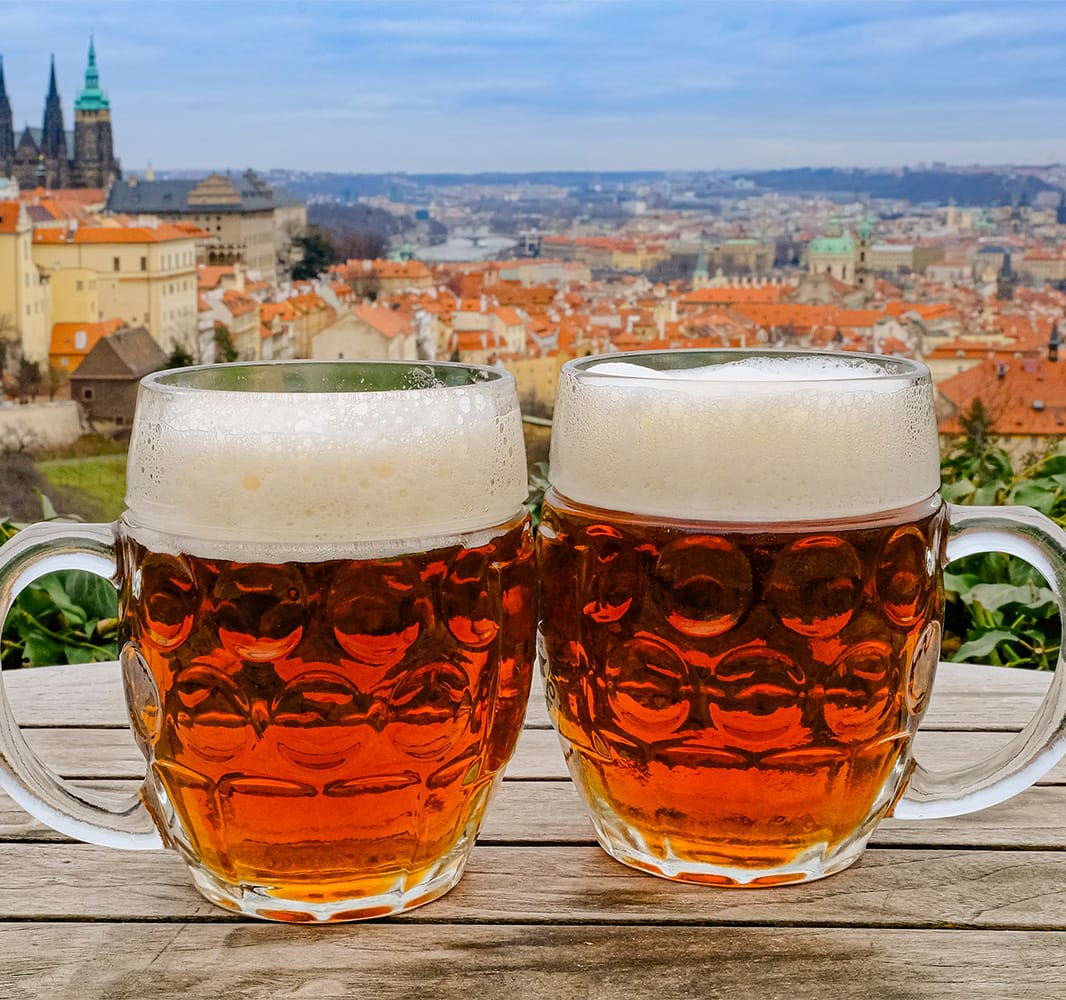 Two glasses of beer on a table with an aerial view of a city in the background