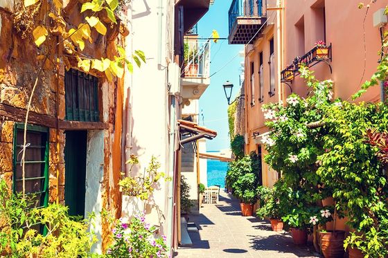 A view from the sidewalk of a colorful beachside town in Greece with plants lining the street