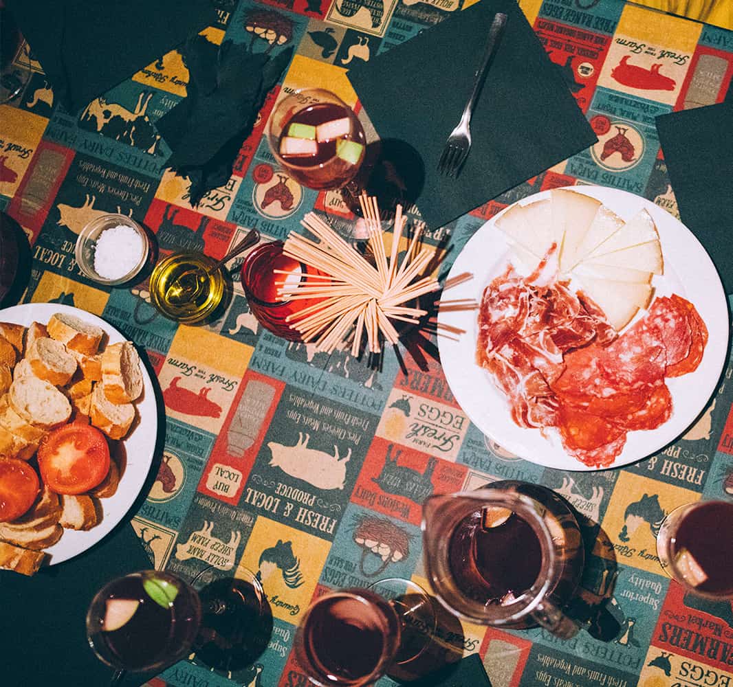 A table with a colorful design covered with plates of smoked meat and cups of sangria