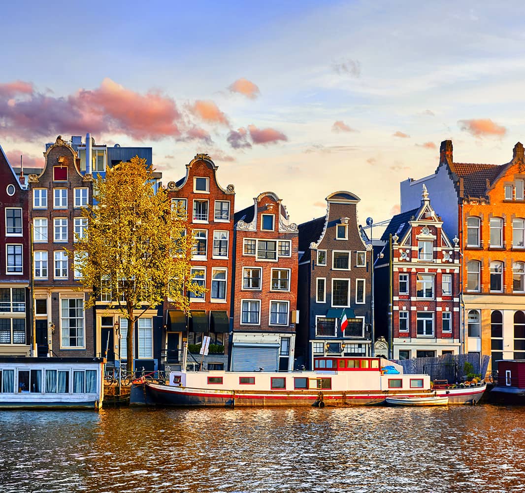 Tall and thin homes that are all unique from each other lined up next to the water with a boat docked in front of the homes