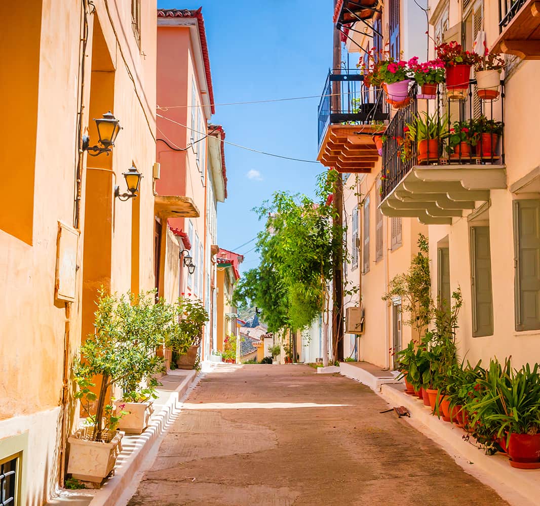 An alleyway with brightly colored buildings on either side and various plants and flowers lining the street