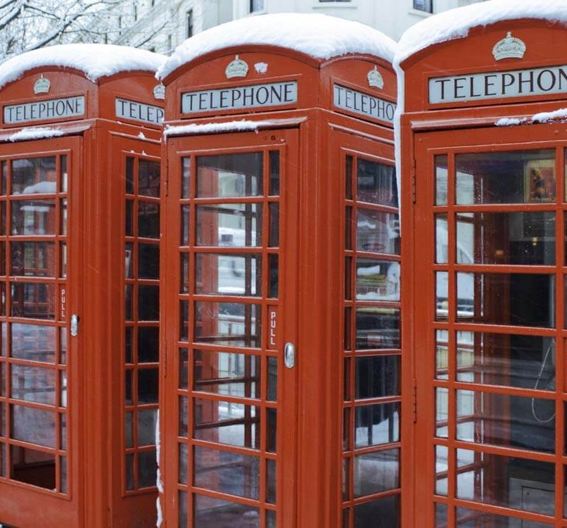 A row of red telephone booths topped with snow