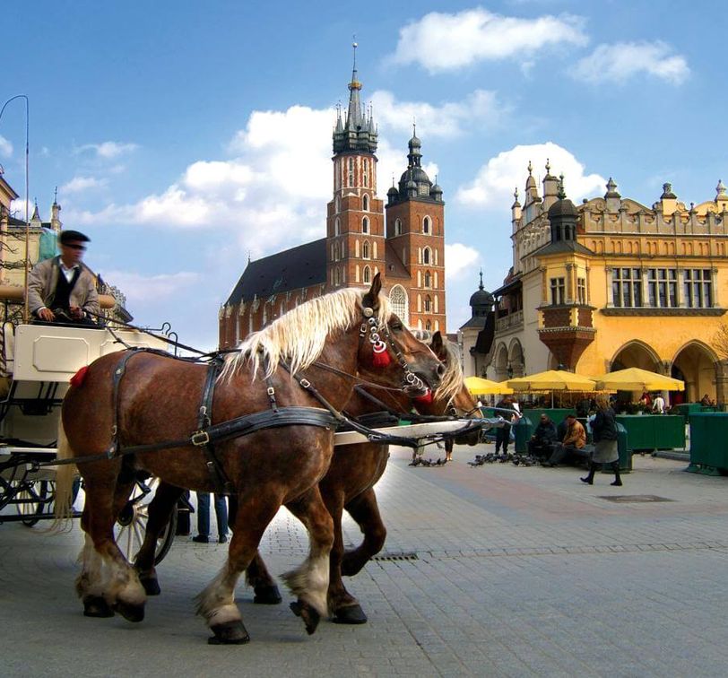 A horse drawn carriage riding through the main square of Krakow.