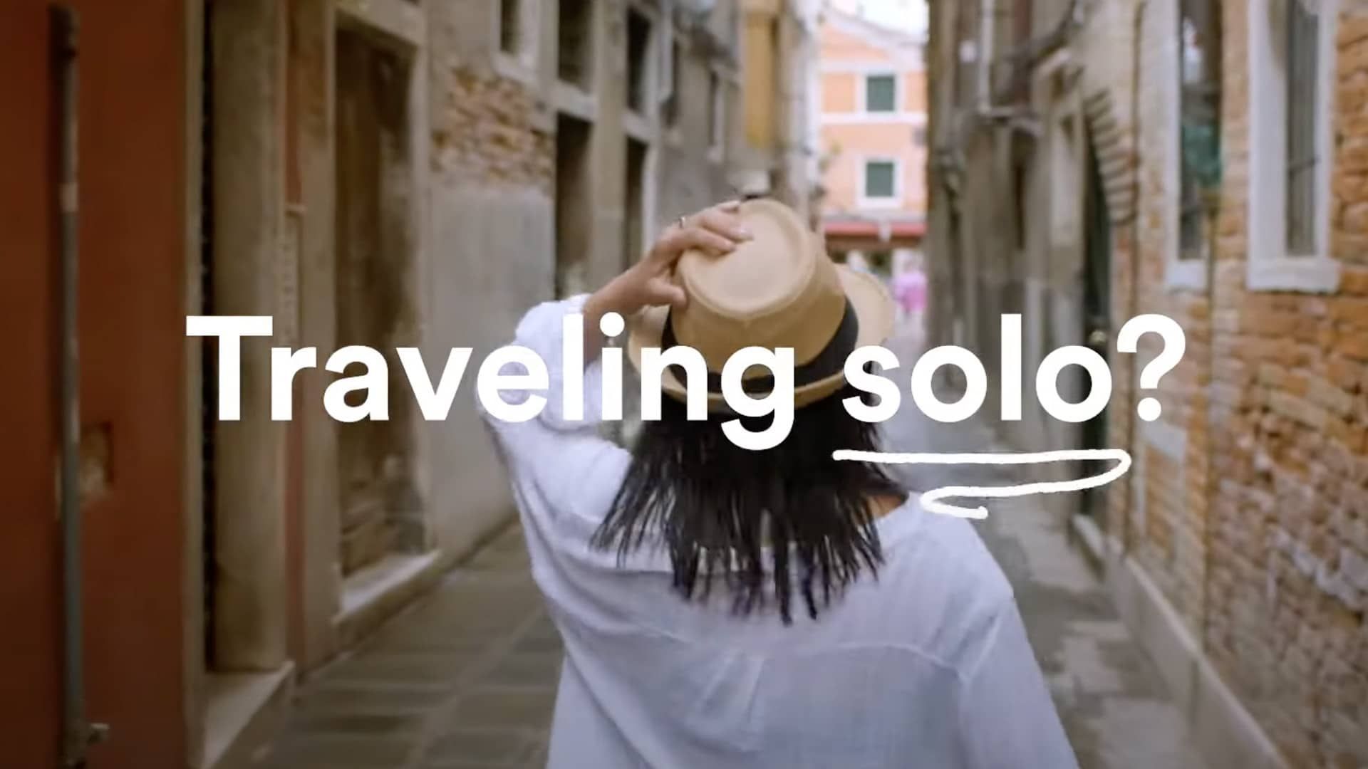 "Traveling solo?” text over a woman in a hat walking alone down a street.