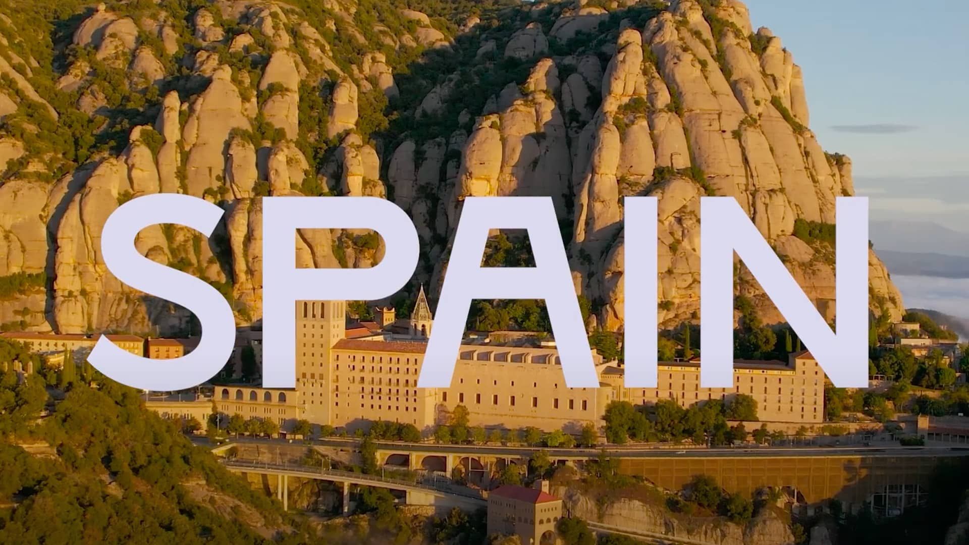 "Spain" text over buildings at the base of a mountain.