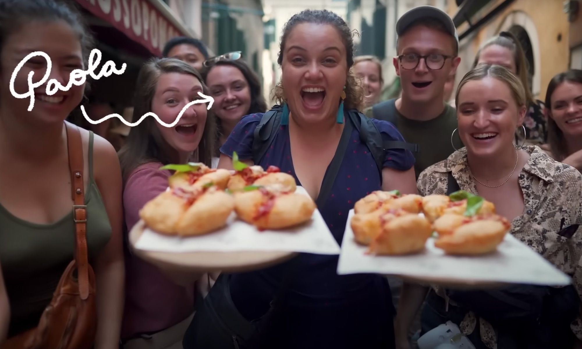 A woman smiling and holding plates of food while others gather around her and look at the food smiling