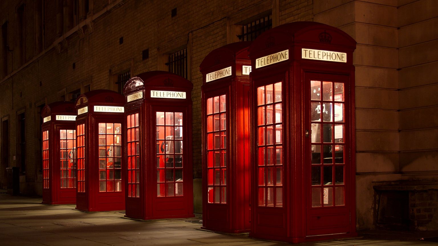 5 lit-up red phone booths in a line in the evening