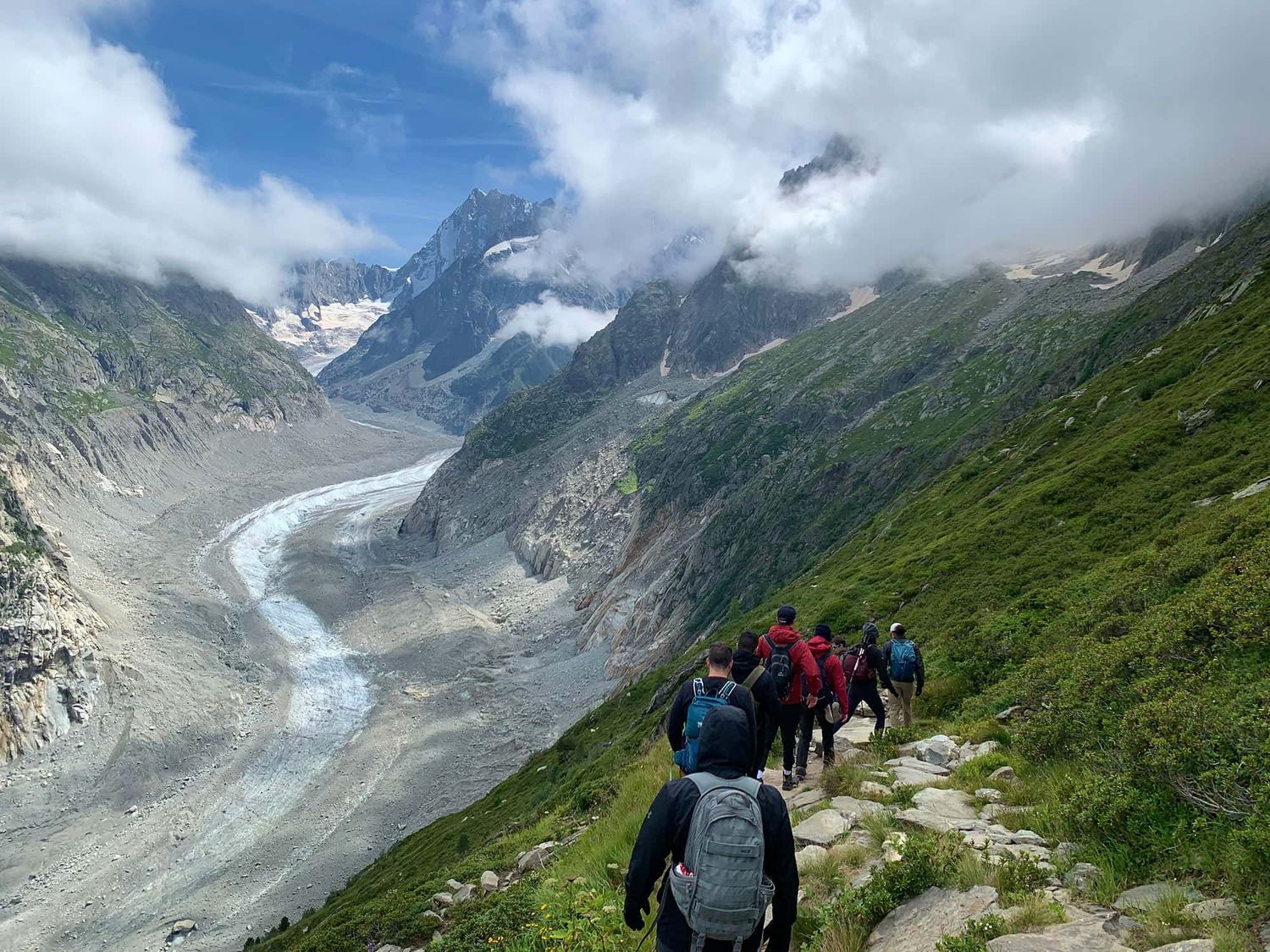 Hikers walking down a rocky path with mountains in the distance.