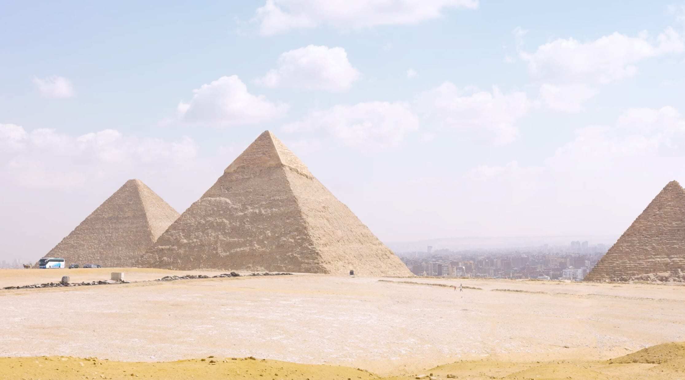 Three large pyramids in the desert overlooking a city in the background on a cloudy day