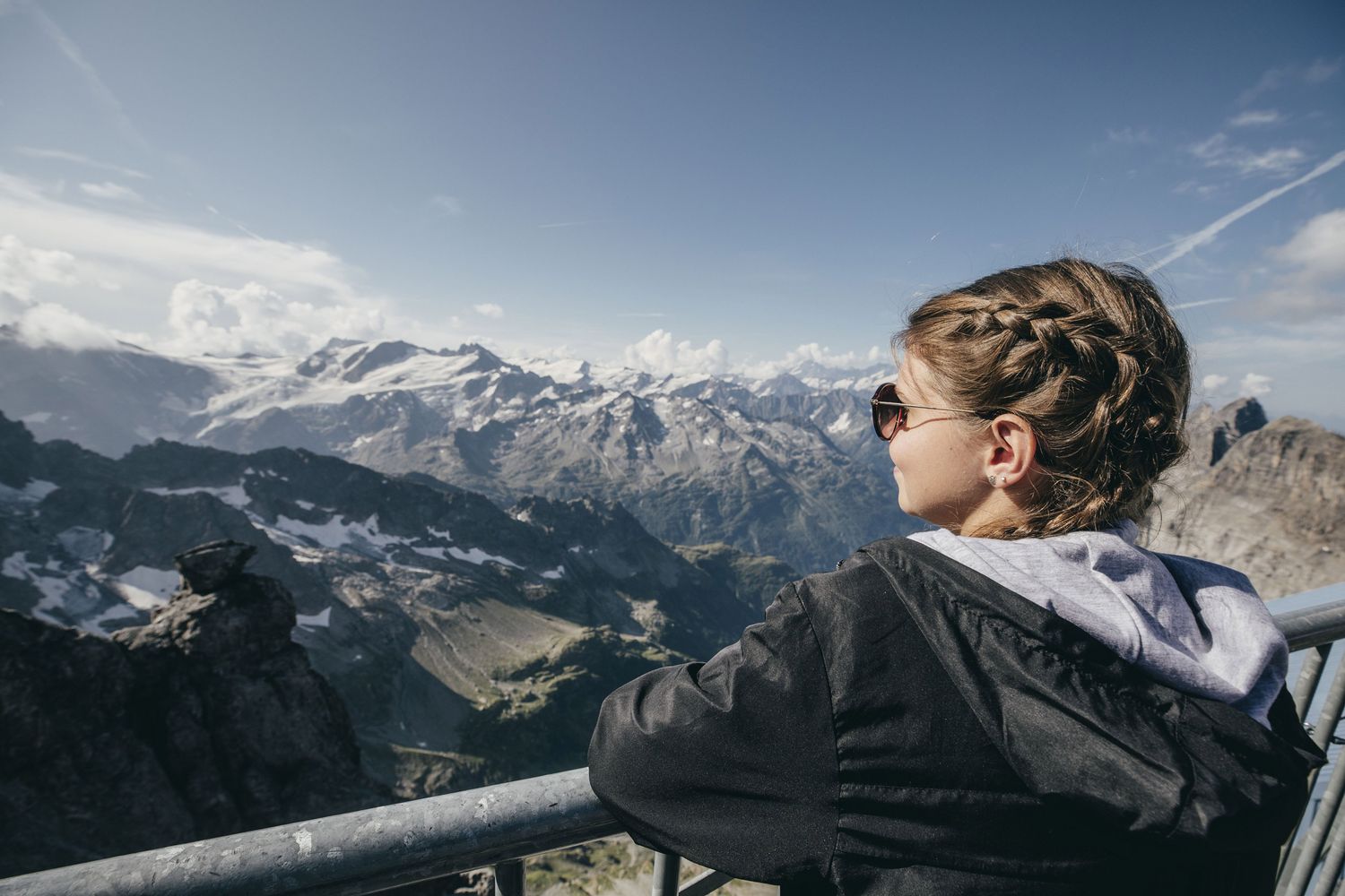 A girl by herself at a viewing platform looking at the Alps in the distance.