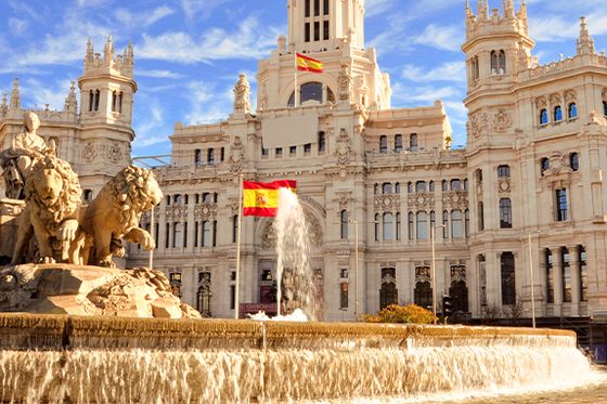 An extremely detailed stone carving of lions and a man in the middle of a water fountain in front of a grand mansion