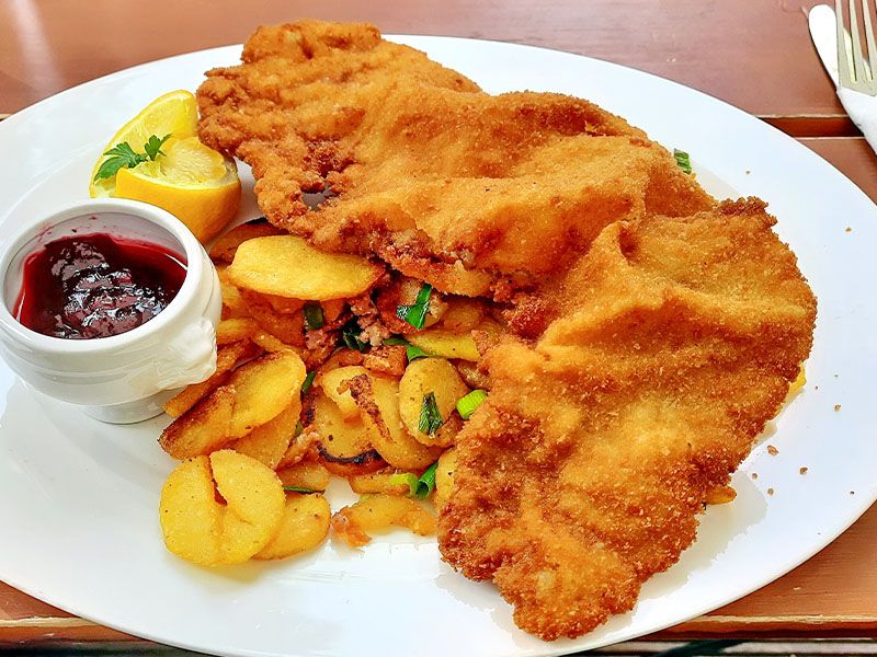 A white plate with schnitzel, potatoes, and a red sauce on the side