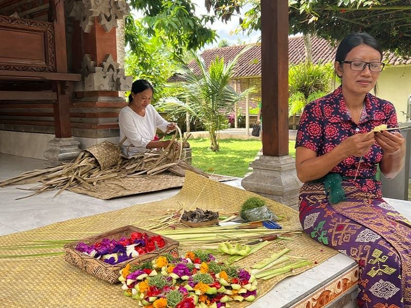 Two women sitting together weaving baskets and handling tropical flowers.