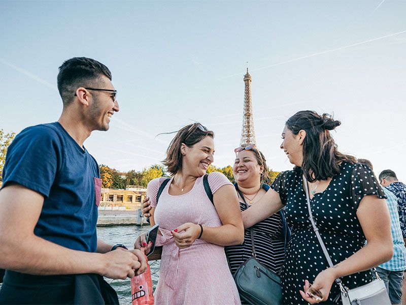 A group of individuals smiling and looking at each other and embracing in front of the Eiffel Tower