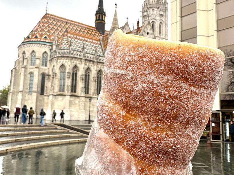 A sugar-covered funnel cake held up in front of a church in the background.