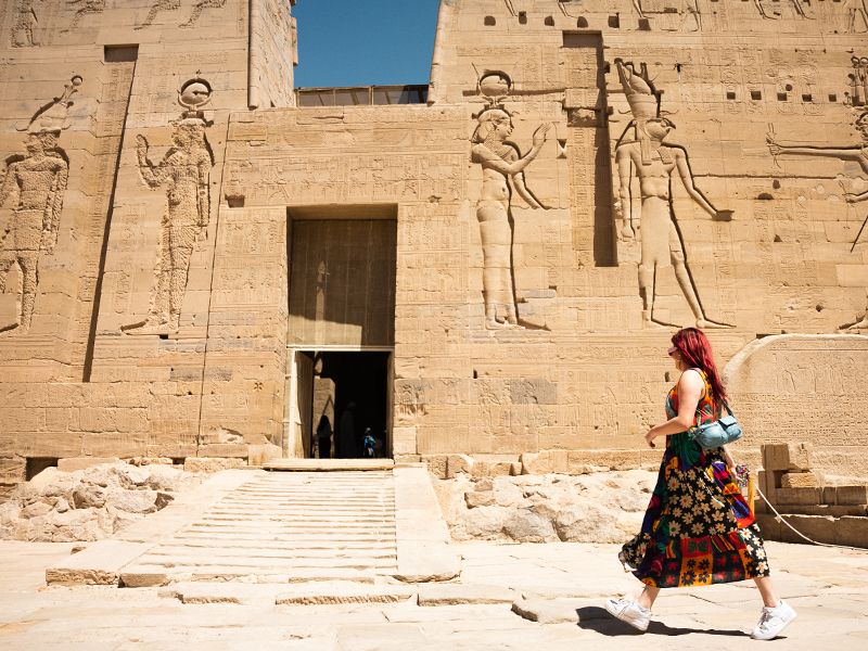 A woman walking toward the entrance of a carved stone temple. 