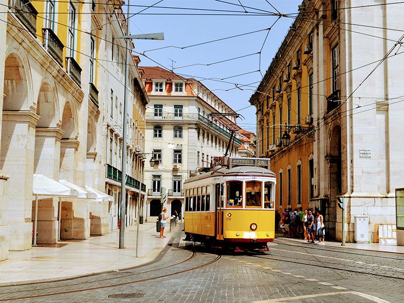 Yellow tram moving through Lisbon street with people wandering around