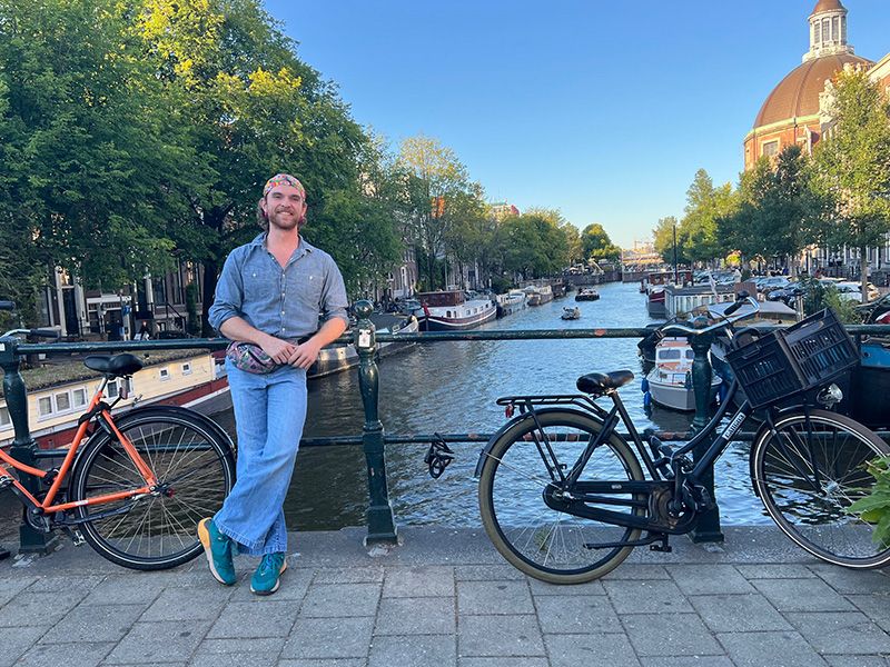 A man standing on a bridge next to two bicycles situated over a tree-lined canal