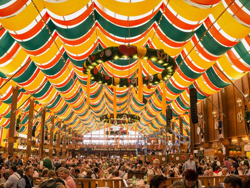 Inside of an Oktoberfest tent with hundred of people sitting at tables drinking beer and chatting