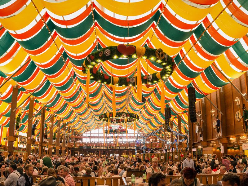 Inside of an Oktoberfest tent with hundred of people sitting at tables drinking beer and chatting