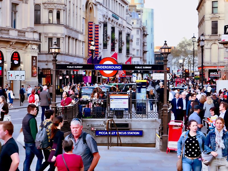 A busy London street with dozens of people and a staircase leading to the London Underground