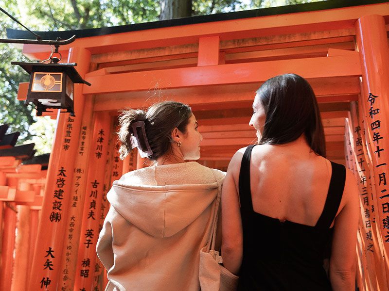 Two women looking at each other while facing an orange Japanese temple.