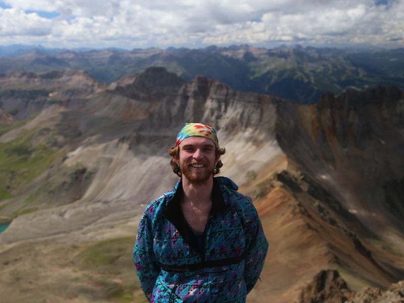 A man smiling for a photo standing in front of a view of mountains and valleys