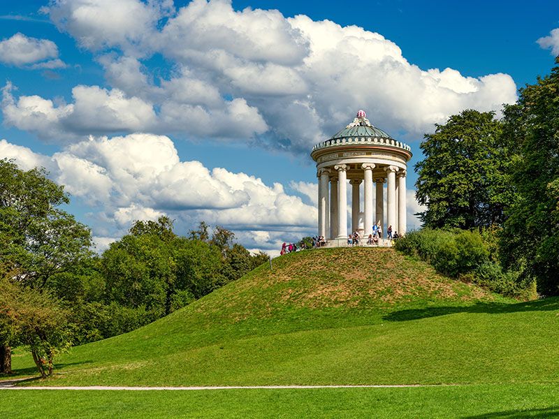 Grassy park with trees and a greek-style temple on a hill