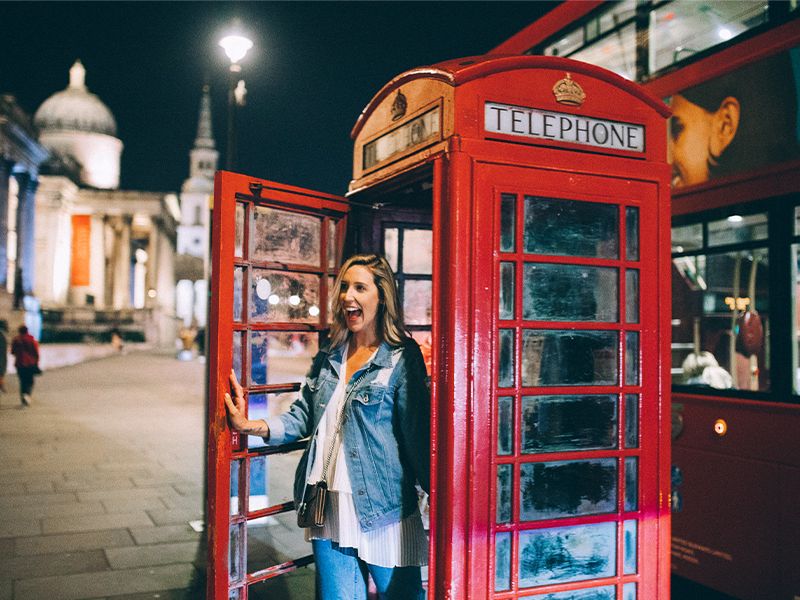 A woman smiling and posing at the door to a red phone booth in London